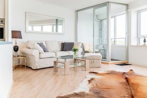 A modern living room with a sofa, coffee table, and glass door leading to a balcony. - Vacation apartment "FjordHavn" on the 8th floor of the Viking Tower (Schleswig)