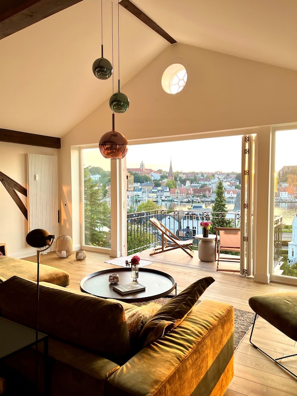 A modern living room with a large window, a round coffee table, a sofa, and a balcony with a view of a cityscape. - "Hafenpanorama" vacation rental with a view of the Old Town and the harbor, located right in (Flensburg)