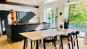 A modern kitchen with a black countertop, wooden dining table, and chairs, a small island with a sink, and a balcony with a view of greenery. - "Hafenpanorama" vacation rental with a view of the Old Town and the harbor, located right in (Flensburg)