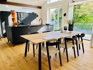 A modern kitchen with a black countertop, wooden dining table, and chairs, a small island with a sink, and a balcony with a view of greenery. - "Hafenpanorama" vacation rental with a view of the Old Town and the harbor, located right in (Flensburg)