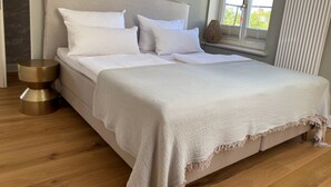 A bed with white bedding, a round bedside table, and a window with blinds. - "Hafenpanorama" vacation rental with a view of the Old Town and the harbor, located right in (Flensburg)