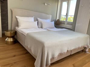 A bed with white bedding, a round bedside table, and a window with blinds. - "Hafenpanorama" vacation rental with a view of the Old Town and the harbor, located right in (Flensburg)