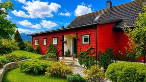 Una casa roja con techo negro, rodeada de vegetación y un cielo despejado.
