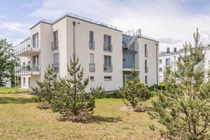 Ein modernes, mehrgeschossiges Wohngebäude mit Balkonen, einer Treppe und einem gepflegten Rasen mit Kiefern.