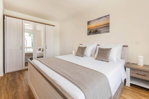 Ein Schlafzimmer mit einem großen Bett, einem Kleiderschrank, einem Nachttisch und einem an der Wand hängenden Gemälde.