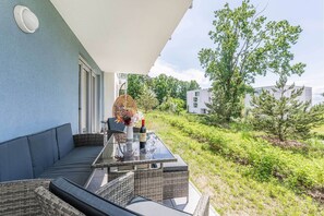 Ein Außenbereich mit einem Glastisch, Korbstühlen und einer Couch.