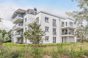 Ein mehrstöckiges Wohngebäude mit Balkonen, einem Garten und blauem Himmel.