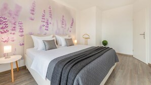 Une chambre à coucher avec un lit, une table de chevet, des œuvres d’art murales et une porte.