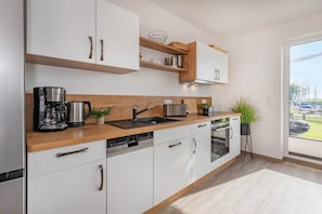 A modern kitchen with white cabinets, wooden countertops, a coffee maker, a toaster, and an oven. - Modern vacation home with lake view, terrace & barbecue in Loddin (Loddin)