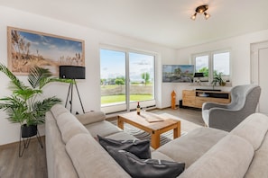 A living room with a sofa, a coffee table, a TV, a plant, and a view of the outdoors.