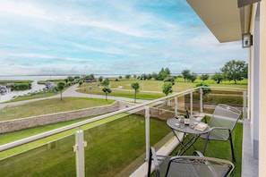 A balcony with a view of a water body, a grassy area, and a paved path.