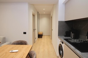 A compact kitchen with a washing machine, a dining area with a table and chairs, and a small bench in the hallway.