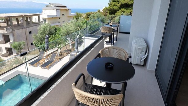 A balcony with a pool, wicker chairs, a table, and a view of the sea and buildings. - Safir Luxury Suites (Sarandë)