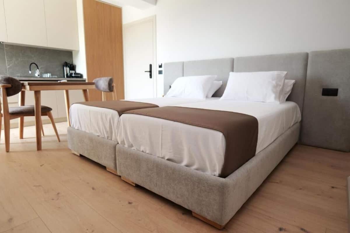 Un dormitorio moderno con cama, mesitas de noche, una silla y una zona de kitchenette.