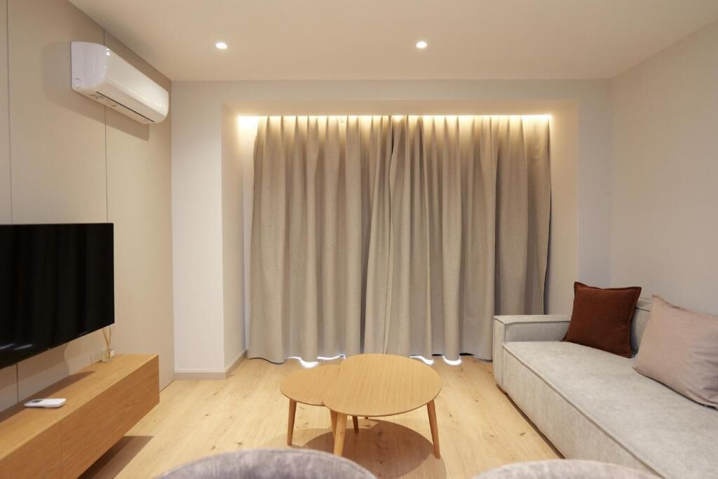 A modern living room with a flat-screen TV, a wooden coffee table, a sofa, and a large window with curtains.