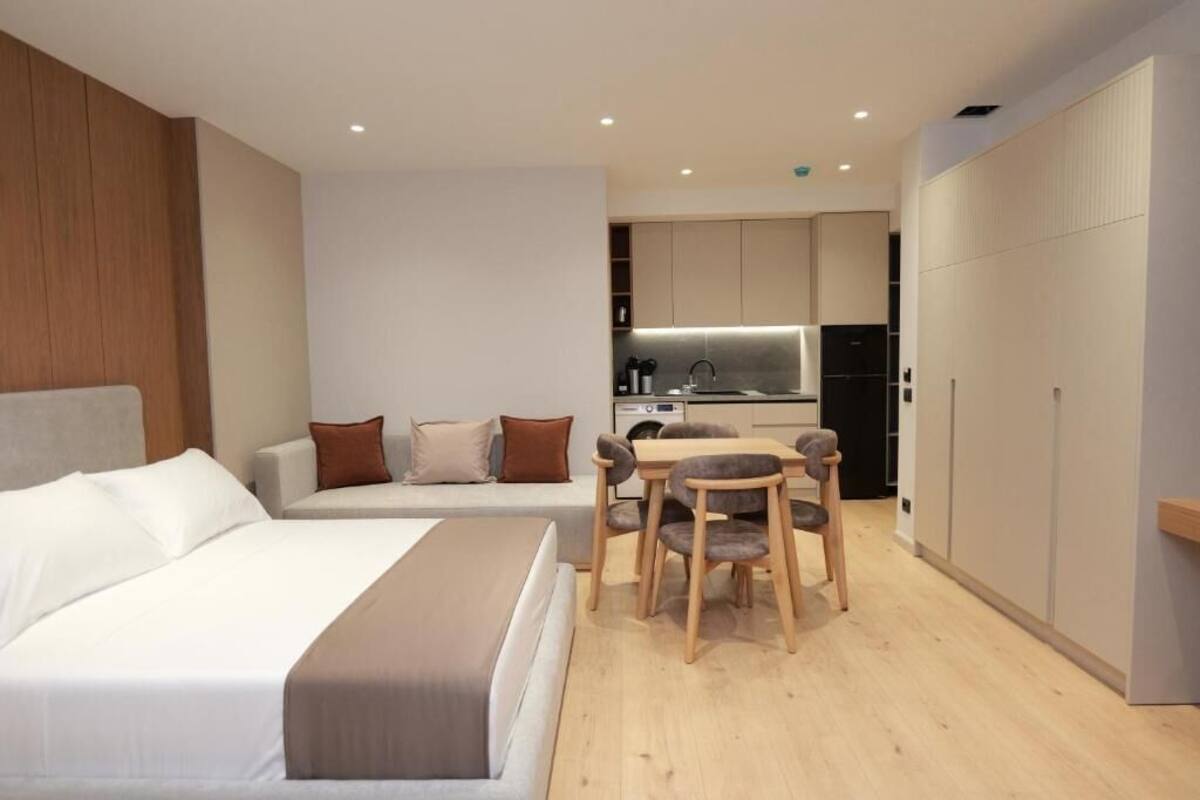 Una habitación de hotel moderna con cama, zona de estar con mesa y sillas, kitchenette y armario.