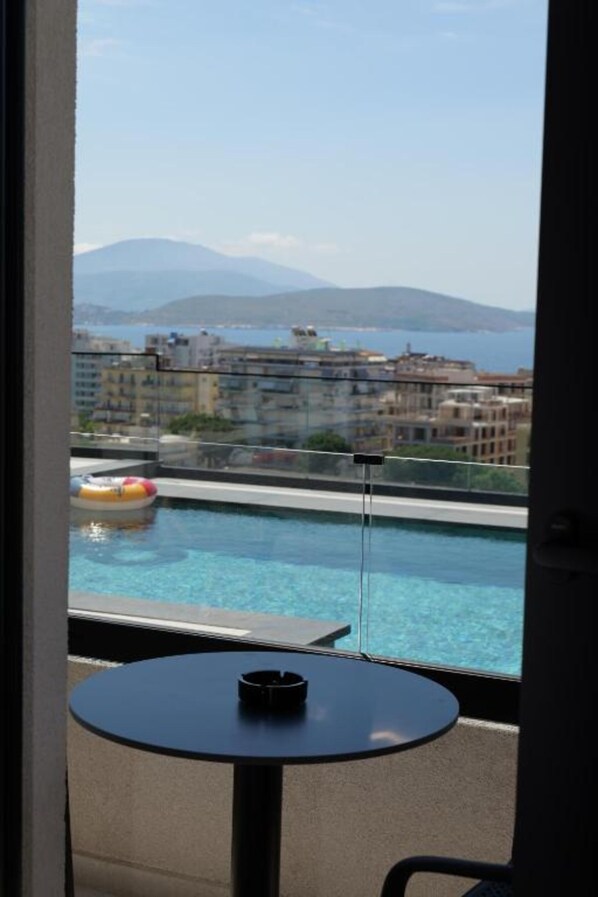 A view from a balcony with a pool, a table, and a view of buildings and mountains.