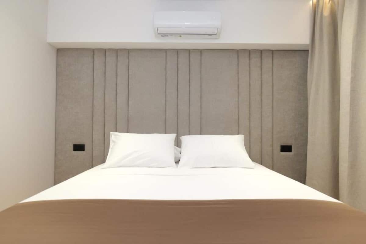Una habitación de hotel con una cama, cabecero, aire acondicionado y cortina.