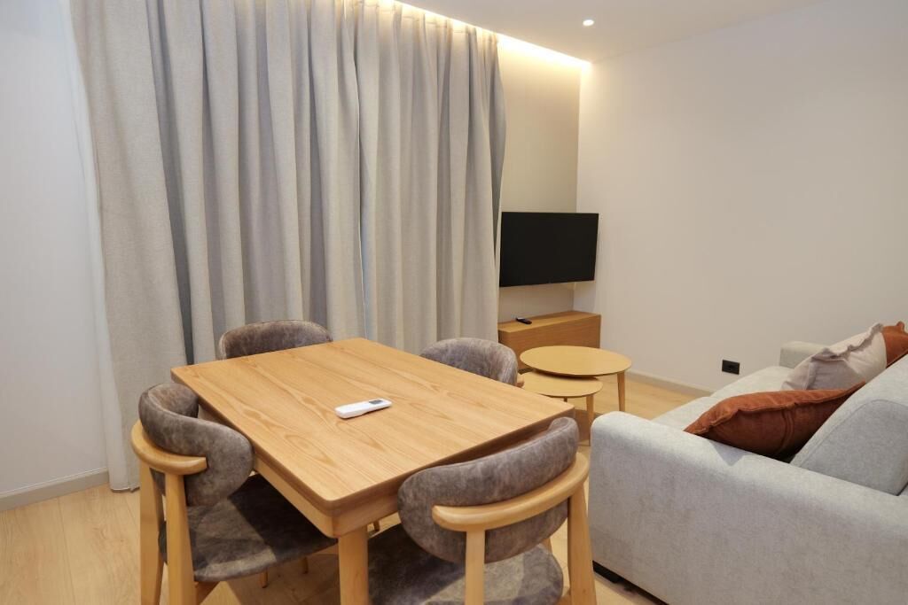 Una sala de estar moderna con una mesa de comedor de madera, sillas tapizadas en gris, un sofá gris, una mesita redonda pequeña y un televisor de pantalla plana montado en la pared.