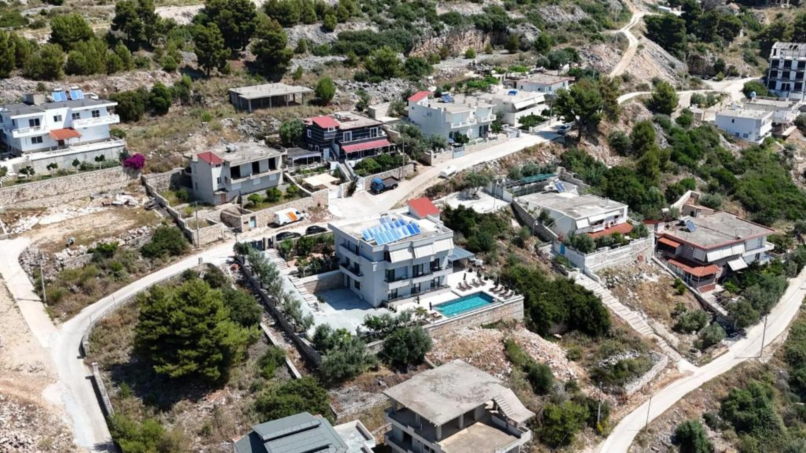 An aerial view of a residential area with multiple buildings, a swimming pool, and surrounding greenery.