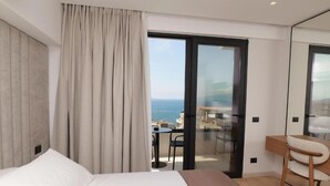 A hotel room with a bed, a desk, a chair, a view of the sea, and a balcony with a table and chairs. - Safir Luxury Suites (Sarandë)