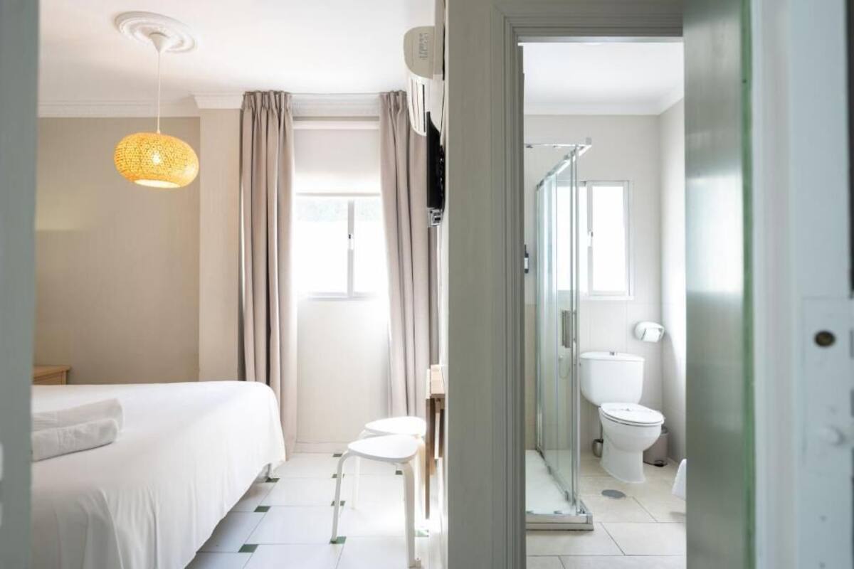 A hotel room with a bed, a small table, a chair, a shower area, and a toilet.