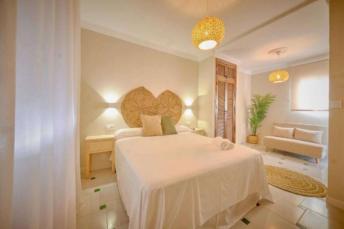 A bedroom with a bed, bedside tables, a wall-mounted light fixture, a potted plant, and a sofa.