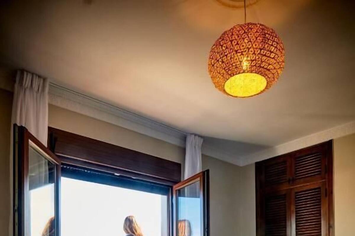 A bedroom with a large bed, a balcony with a view, and a hanging light fixture.