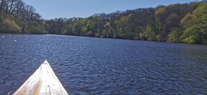 Ein ruhiger See mit einem hölzernen Boot im Vordergrund und einer bewaldeten Uferlinie im Hintergrund.