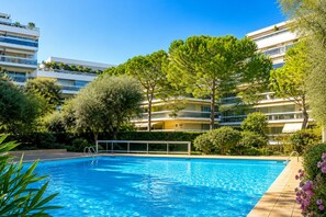 A swimming pool surrounded by greenery and modern buildings. - Studio cabin with pool, terrace, near beaches and Juan-les-Pins center (Antibes)
