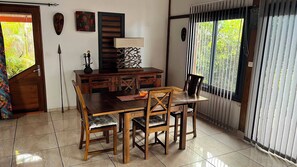 A dining area with a wooden table and chairs, a decorative lamp, and a view through the window. - Villa TheOceane (Les Avirons)