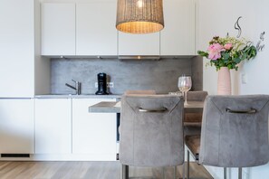 A modern kitchen with white cabinets, a coffee machine, a wine glass, and a wicker pendant light. - White Villa Grömitz apartment 11. sea view. Balcony. Close to the beach (Grömitz)