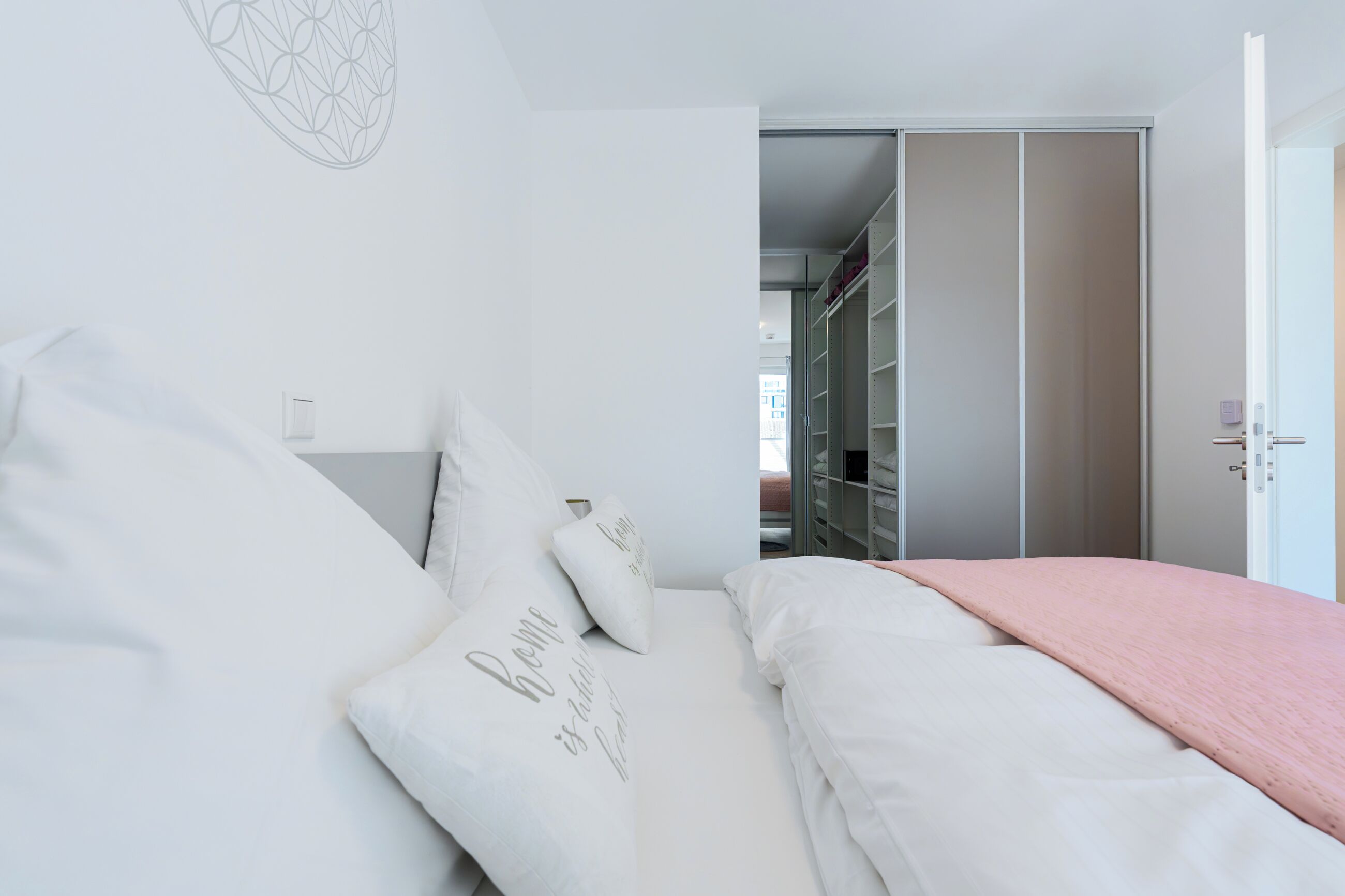 A bedroom with a bed, pillows, a bedside table, a closet, and a door.