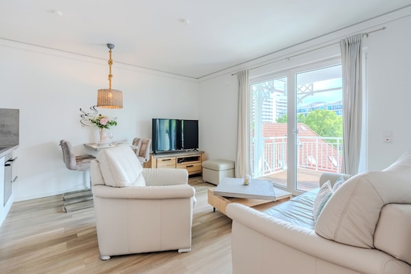Ein modernes Wohnzimmer mit Flachbildfernseher, einer Couch, einem Couchtisch und einem Balkon mit Blick.