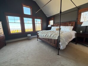A bedroom with a four-poster bed, large windows, a bedside table, and a lamp.