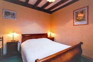 Un dormitorio con una cama de madera, dos mesitas de noche con lámparas, una silla y dos cuadros enmarcados en las paredes.
