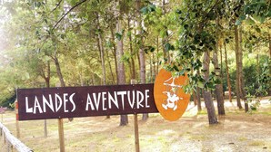 Un letrero que dice 'LANDES AVENTURE' con un logotipo, rodeado de árboles y una valla de madera.