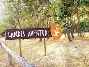 A sign for 'LANDES AVENTURE' with a logo, surrounded by trees and a wooden fence. - Holiday Home With Swimming Pool (Sainte-Eulalie-en-Born)