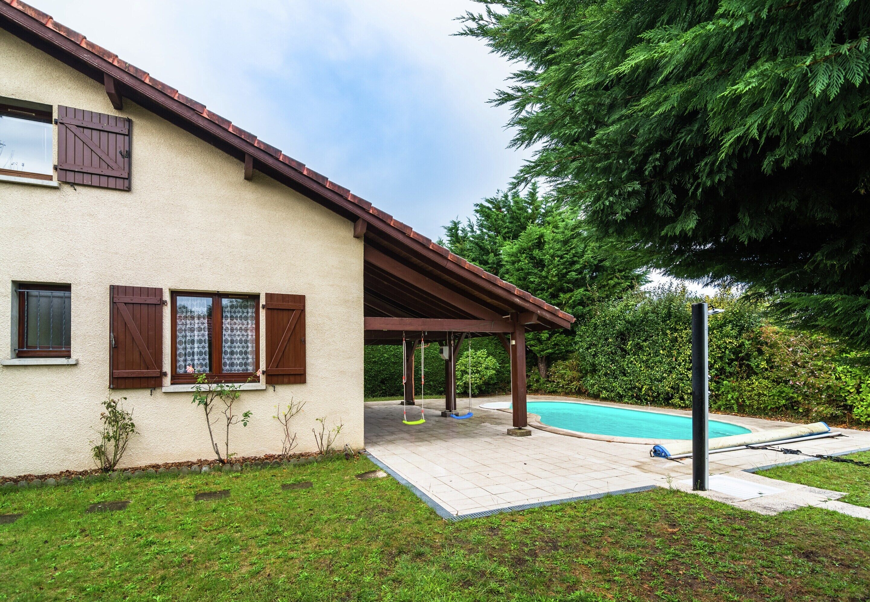 A house with a covered patio, a swimming pool, and a lawn.