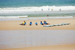A beach with people sitting and standing, some with surfboards. - Holiday Home With Swimming Pool (Sainte-Eulalie-en-Born)