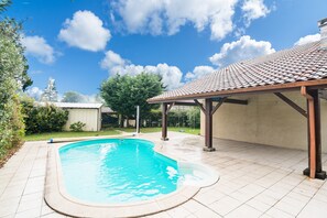 Una piscina con solana empedrada, un porche cubierto y un cielo azul despejado.