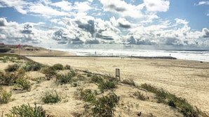 Una playa con dunas de arena, cielo despejado y el océano al fondo.