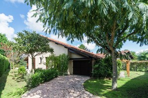 A house with a paved driveway, a garage, and a garden with various plants and trees. - Holiday Home With Swimming Pool (Sainte-Eulalie-en-Born)