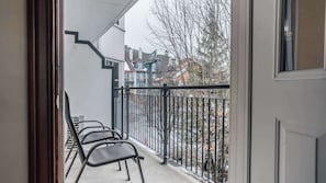 Ein Balkon mit Metallstühlen, einem schwarzen Metallgeländer und Blick auf Gebäude und Bäume.