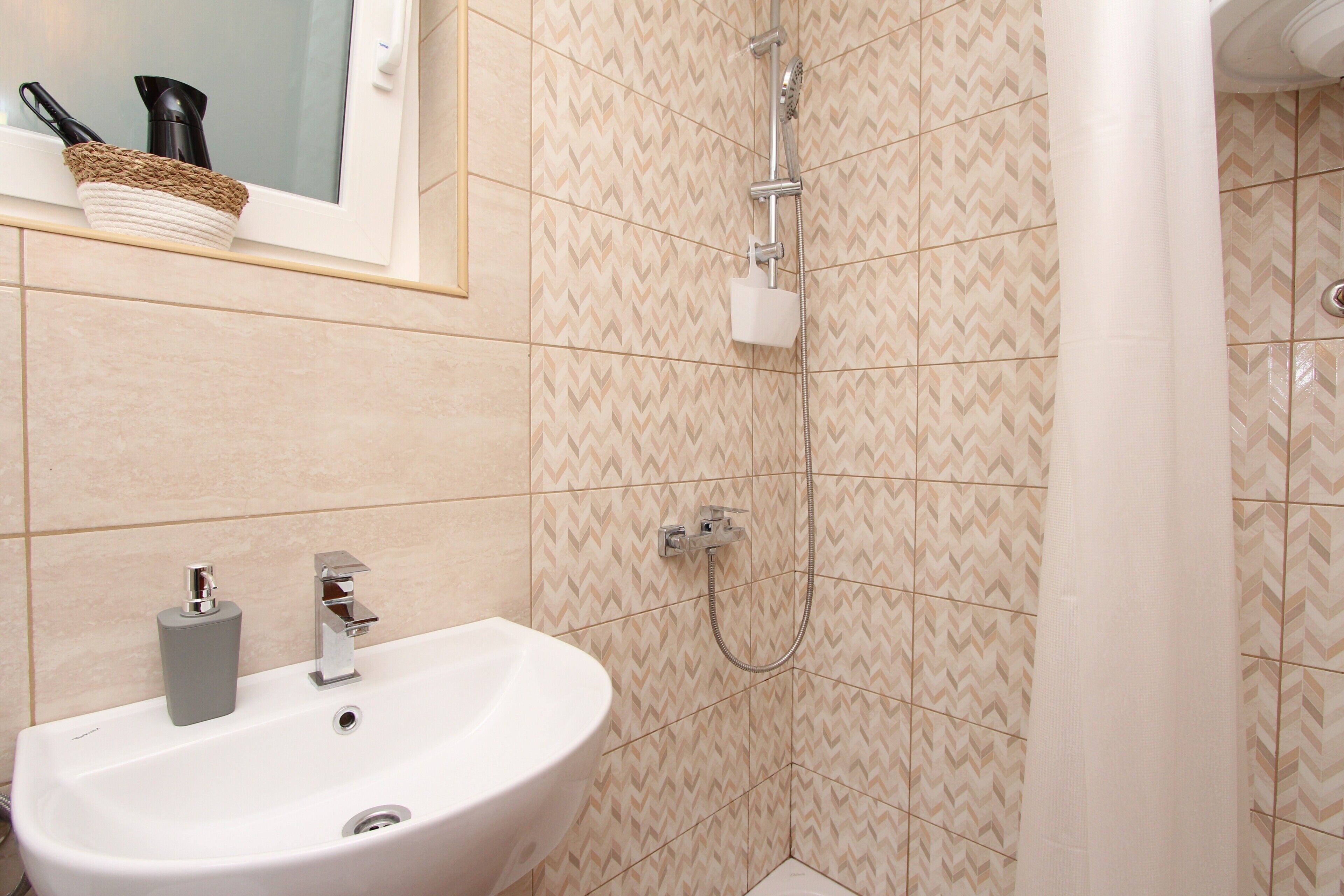 A bathroom with a sink, mirror, and shower.