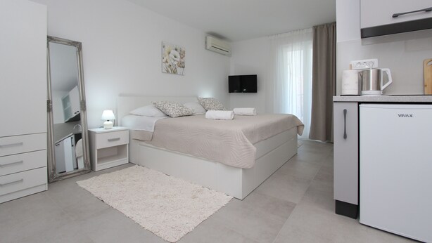 A bedroom with a bed, bedside table, lamp, and a white refrigerator. - Room and Studios Sole (Rovinj)