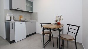 A compact kitchen with a dining table and chairs, a coffee machine, and a small cabinet. - Room and Studios Sole (Rovinj)