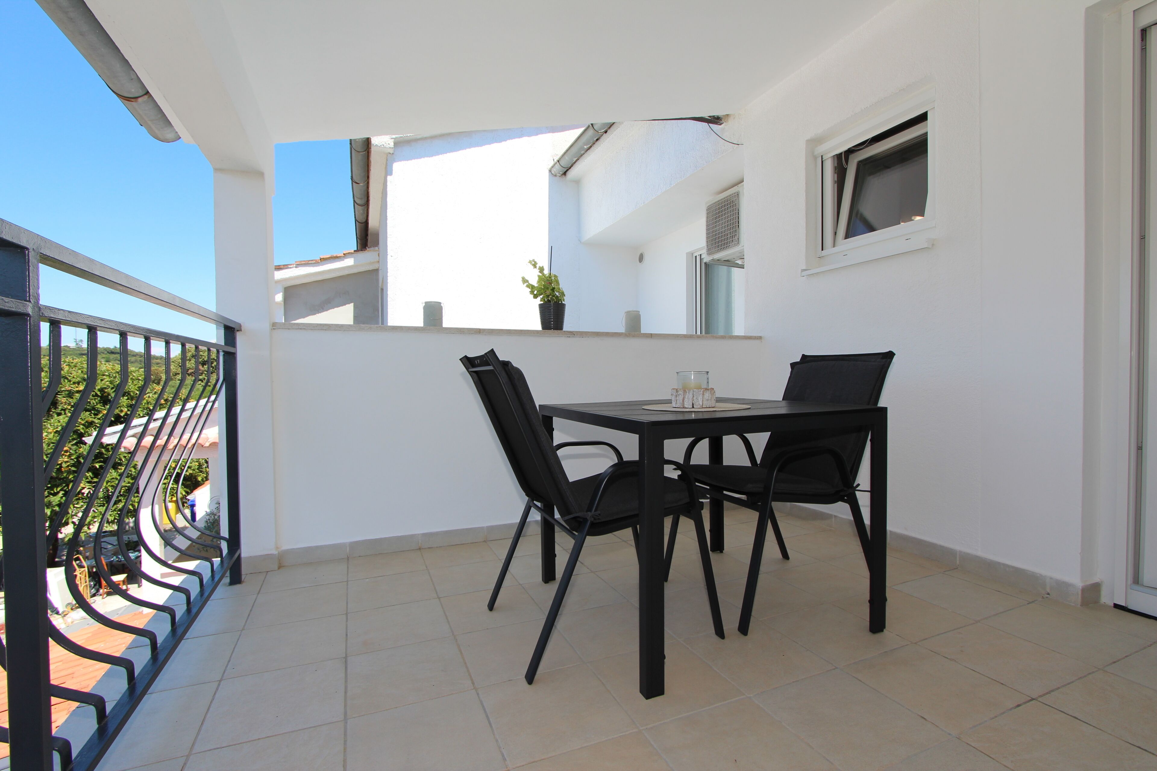 Een balkon met een tafel en stoelen, een plant in pot en een raam.