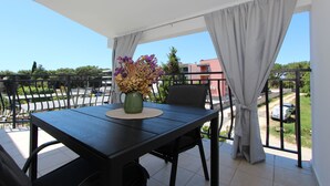 A balcony with a table, a chair, a vase with flowers, and a view of the street and buildings. - Room and Studios Sole (Rovinj)