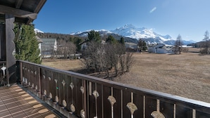 A balcony with a view of a snow-capped mountain, a wooden fence, and a clear sky.